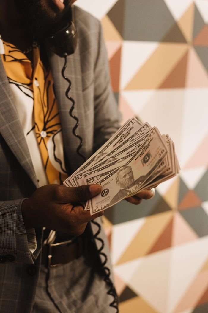 Close-up of a man holding US dollar bills while talking on a vintage phone indoors.